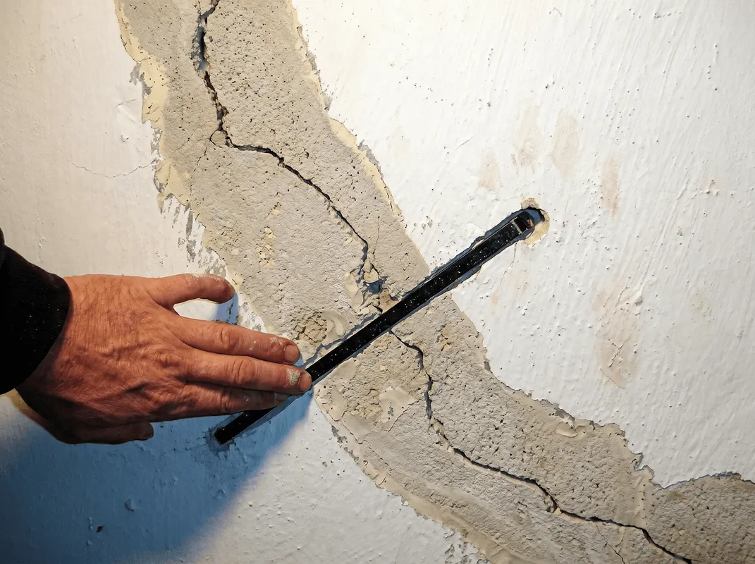 A wall with a large crack is being inspected by a professional in Peoria, IL